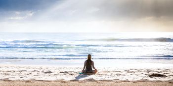 Mujer sentada en posición de loto en la orilla de una playa